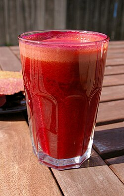Glass of beetroot juice beside fresh beets and greens on a rustic table