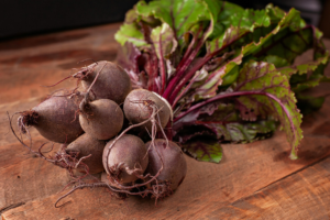 Bowl of whole beets with attached greens on a wooden table