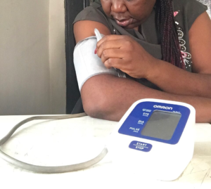 “Person using a home digital blood pressure monitor at a table.”