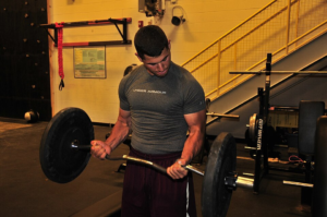 Person lifting a barbell in a gym with free weights.”