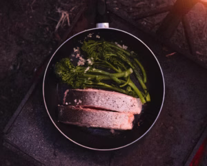 “Salmon fillets cooking in a pan with greens and lemon slices”