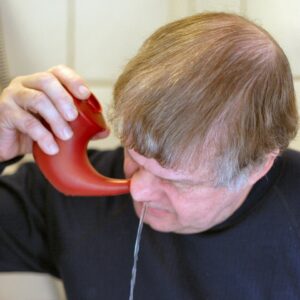 person performing nasal saline irrigation with rinse pot